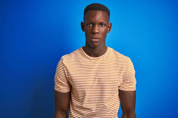アフリカ系アメリカ人男性は 青い背景に真剣な表情で立つストライプのカジュアルなTシャツを着ている カメラを見てシンプルで自然な — ストック写真