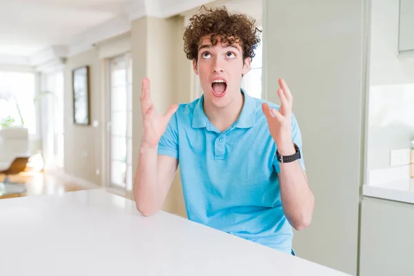 自宅でカジュアルな青いTシャツを着た若いハンサムな男は 攻撃的な表情と腕を上げて怒鳴り 叫びました 欲求不満の概念 — ストック写真