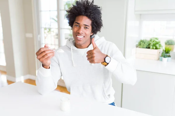African American man eating healthy yogurt for breakfast happy with big smile doing ok sign, thumb up with fingers, excellent sign