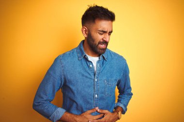 Genç Hint adam kot gömlek ayakta izole sarı arka plan üzerine el mide nedeniyle hazımsızlık, ağrılı hastalık duygusunu hissediyorum. Ağrı kavramı.