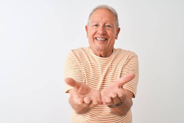 Üst düzey gri saçlı adam çizgili t-shirt izole beyaz arka plan üzerinde duran giyen birlikte alma veya jest veren avuç içi ile gülümseyerek. Tutma ve koruma