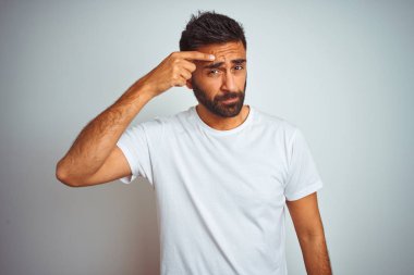 Genç Hint adam giyen t-shirt ayakta izole beyaz arka plan üzerinde sivilce için mutsuz işaret alnında, çirkin enfeksiyon siyah kafa. Akne ve cilt sorunu