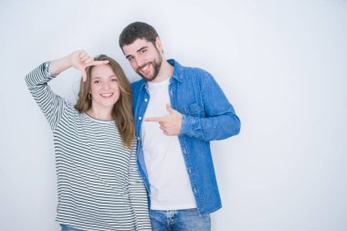 Beyaz izole arka plan üzerinde birlikte ayakta genç güzel çift mutlu yüz ile eller ve parmaklar ile çerçeve yapma gülümseyen. Yaratıcılık ve Fotoğrafçılık konsepti.