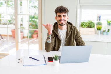 Bilgisayar laptop ve işaret ve başparmak kadar mutlu yüz gülümseyen tarafı ile gösterilen defter kullanan genç öğrenci adam