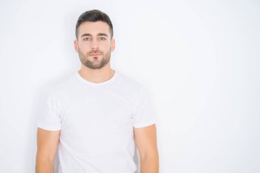 Yüzünde ciddi bir ifade ile beyaz izole arka plan üzerinde rahat beyaz t-shirt giyen genç yakışıklı adam. Basit ve doğal kamera bakıyor.