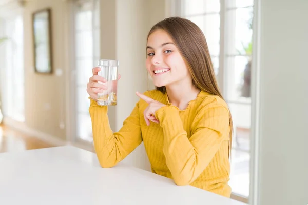 美丽的年轻女孩孩子喝一杯新鲜的水很高兴指着手和手指 — 图库照片