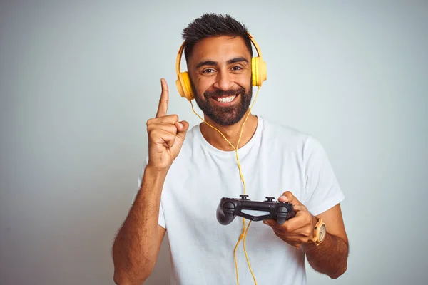 孤立した白い背景の上にヘッドフォンを使用してビデオゲームをプレイするアラブのインドのゲーマーの男は 幸せな顔で指を指すアイデアや質問に驚きました ナンバーワン — ストック写真