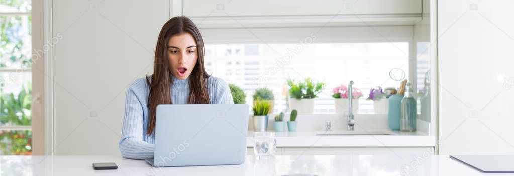 Wide angle picture of beautiful young woman working or studying using laptop scared in shock with a surprise face, afraid and excited with fear expression