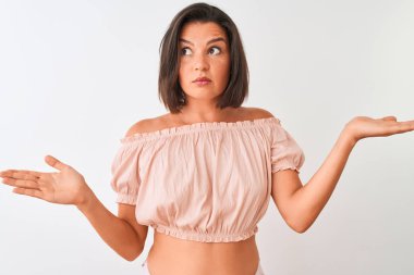 Genç güzel kadın rahat t-shirt izole beyaz arka plan üzerinde duran giyen habersiz ve kolları ve elleri ile karışık ifade kaldırdı. Şüphe kavramı.