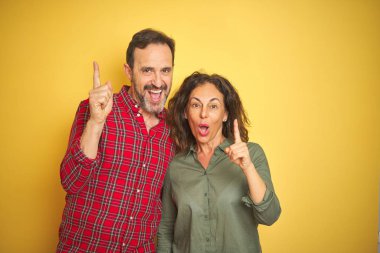 İzole sarı arka plan üzerinde güzel orta yaş çift başarılı bir fikir ile parmak yukarı işaret. Çıkıldı ve mutlu. Bir numara.