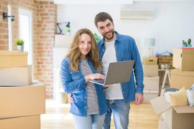 Yeni bir daireye taşımak için mutlu karton kutular etrafında bir odada bilgisayar laptop ayakta kullanarak genç çift