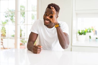 Afro-Amerikan yakışıklı beyaz tablo evde gülümseyerek el parmakları ile mutlu yüz üzerinden seyir göz ile ok jest yapıyor.