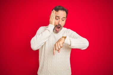 İzole kırmızı arka plan üzerinde gri saçlı yakışıklı Orta Çağ kıdemli adam saat zaman endişeli, geç olmaktan korkuyor bakıyor