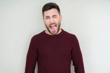 Genç yakışıklı adam izole arka plan üzerine bir kazak giyiyor dil komik ifade ile mutlu yapışıyor. Duygu konsepti.