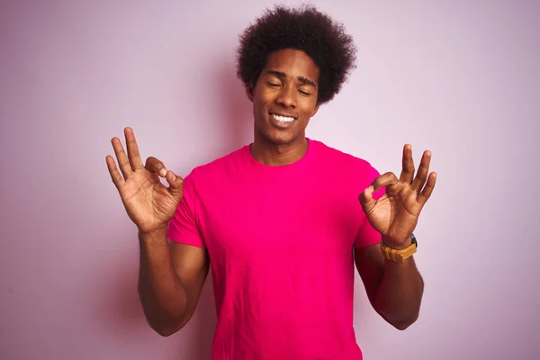 年轻的美国男子 一个非洲的头发 穿着T恤站在孤立的粉红色背景放松和微笑与眼睛闭着手指做冥想手势 瑜伽概念 — 图库照片