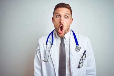 İzole arka plan üzerinde beyaz profesyonel ceket giyen genç yakışıklı Doktor adam korkuyor ve sürpriz ifade, korku ve heyecanlı yüz ile şok.