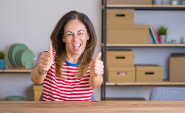 Evde masada oturan orta yaş kıdemli kadın el ile olumlu jest yapıyor onayladı, gülümseyen ve başarı için mutlu kadar başparmak. Kazanan jest.