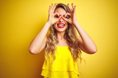 Genç attactive kadın giyen t-shirt sarı izole arka plan üzerinde ayakta dil yapışan dürbün gibi ok jest yapıyor, gözleri parmaklarla bakıyor. Çılgın ifade.