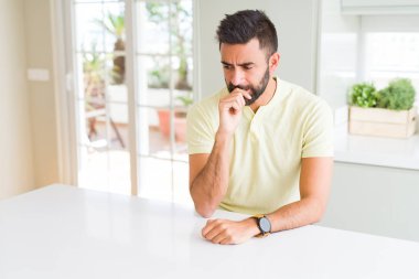 Evde yakışıklı İspanyol adam rahat sarı t-shirt vurguladı ve ağız ısırma çivi elleri ile gergin bakıyor. Anksiyete sorunu.