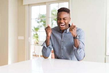 Beyaz masada yakışıklı Afrikalı Amerikan adam silah ile başarı için heyecanlı kutlamak zafer gülümseyen kaldırdı. Kazanan kavramı.