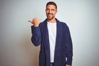 Genç adam rahat pijama ve bornozu sabah izole arka plan üzerinde mutlu yüz görünümlü ve başparmak ile yan işaret ile gülümseyen üzerinde giyiyor.