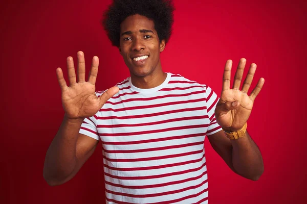 孤立した赤い背景の上にストライプのTシャツを着たアフロヘアの若いアフリカ系アメリカ人男性は 自信を持って幸せに微笑みながら 指番号9を示し 指を上げている — ストック写真
