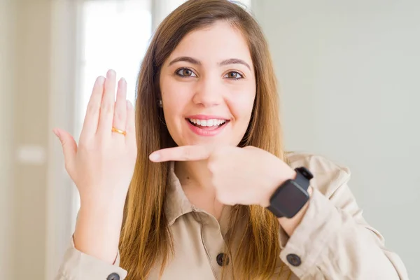 Beautiful young woman showing alliance ring on hand very happy pointing with hand and finger