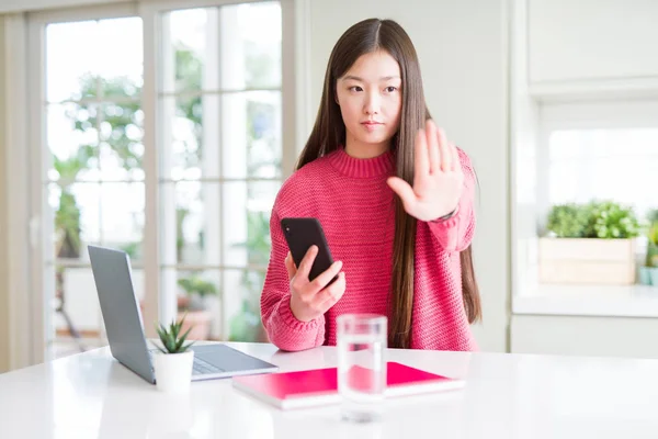 美丽的亚洲学生妇女使用笔记本电脑和智能手机与打开的手做停止标志与认真和自信的表情 防御手势 — 图库照片