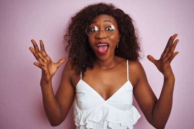 Genç Afrikalı Amerikalı kadın izole pembe arka plan üzerinde ayakta giyen gözlük deli kutluyor ve başarı için hayran silah kaldırdı ve açık gözleri heyecanlı çığlık. Kazanan kavramı