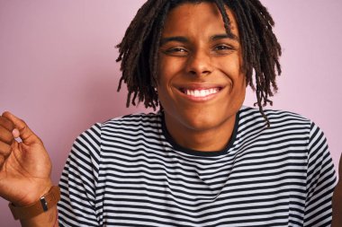 Zencili pembe arka plan üzerinde lacivert çizgili t-shirt giyen dreadlocks ile Afro Amerikan adam gururlu çığlık ve zafer kutluyor ve başarı çok heyecanlı, tezahürat duygu