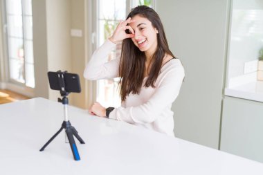 Güzel genç kadın kayıt selfie video ile akıllı telefon Webcam ile mutlu yüz gülümseyen ok işareti ile elle görünümlü göz parmaklar