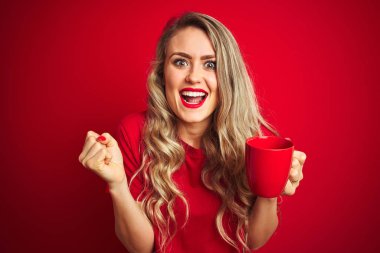 Young beautiful woman drinking a cup of cooffe over red isolated background screaming proud and celebrating victory and success very excited, cheering emotion clipart
