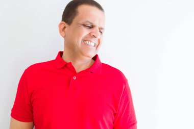 Orta yaş adam beyaz duvar üzerinde kırmızı t-shirt giyen yüzünde gülümseme ile yan bakmak, doğal ifade. Güven gülüyor.