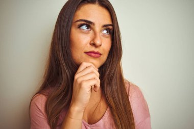 Genç güzel kadın izole beyaz arka plan üzerinde ayakta pembe tişört giyen soru hakkında düşünme ciddi yüz, çok karışık fikir