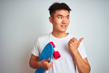 Genç Asya Çinli öğrenci adam tutan paten ayakta izole beyaz arka plan işaret ve gösteren başparmak ile yan kadar mutlu yüz gülümseyen