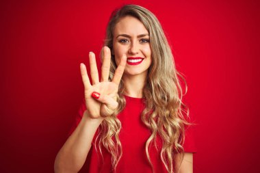 Kırmızı izole arka planda duran temel t-shirt ayakta giyen genç güzel kadın ve emin ve mutlu gülümseyen süre dört parmak sayısı ile işaret.