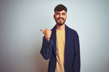 Dövme ile genç adam izole beyaz arka plan üzerinde ayakta elbise giymek mutlu yüz görünümlü ve başparmak ile yan işaret ile gülümseyen.