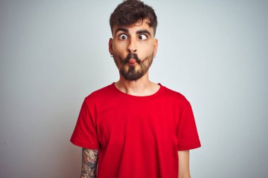 Dövme ile genç adam kırmızı t-shirt ayakta izole beyaz arka plan üzerinde dudaklar ile balık yüz yapma, deli ve komik jest. Komik ifade.