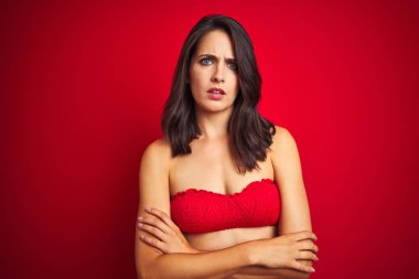 Kırmızı izole arka planda şüpheci ve sinir üzerinde bikini mayo giyen güzel bir kadın, Çapraz kollar ile yüz üzerindeki ifade onaylamıyor. Negatif kişi.