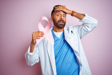 Genç Hint Doktor adam tutan kanser şerit ayakta izole pembe arka plan üzerinde el ile vurguladı, utanç ve sürpriz yüz ile şok, öfkeli ve sinirli. Korku ve hata için üzgün.