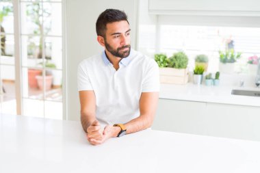 Evde yan arayan yakışıklı İspanyol adam Casual beyaz t-shirt, güvenli bir gülümseme ile doğal yüz ile profil poz rahatlayın.