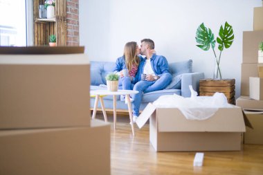 Genç çift etrafında karton kutular ile yeni bir ev kanepede oturan kahve bir fincan içme rahatlatıcı, çok mutlu yeni bir daireye hareket