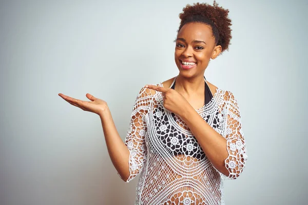 Young african american woman with afro hair wearing a bikini over white isolated background amazed and smiling to the camera while presenting with hand and pointing with finger.