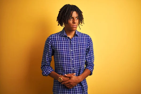 Afro man with dreadlocks wearing casual shirt standing over isolated yellow background with hand on stomach because nausea, painful disease feeling unwell. Ache concept.
