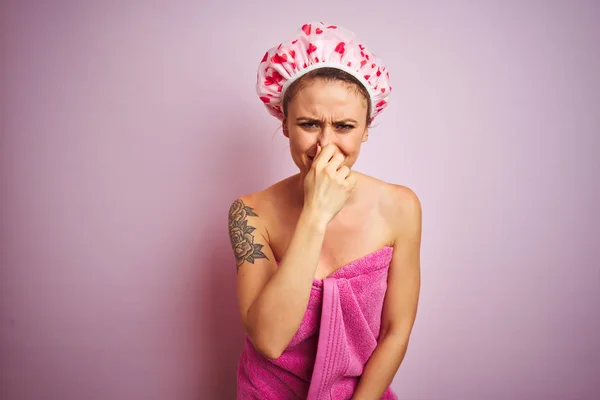 年轻的漂亮女人穿着毛巾和浴帽淋浴后 粉红色孤立的背景闻到一些臭气熏天 无法忍受的气味 用手指在鼻子上屏住呼吸 臭味概念 — 图库照片