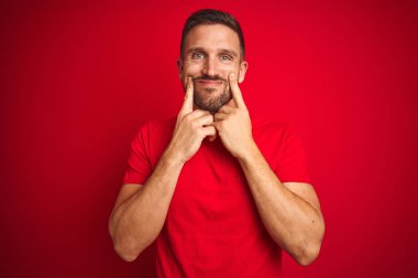 Kırmızı izole arka planda rahat t-shirt giyen genç yakışıklı adam açık ağız ile gülümseyen, parmaklar işaret ve neşeli gülümseme zorlayarak