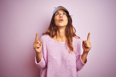 Pembe izole arka plan üzerinde ayakta komik kedi kap giyen genç güzel kadın şaşırdı ve görünümlü ve parmaklar ve yükseltilmiş kollar ile işaret şaşırttı.