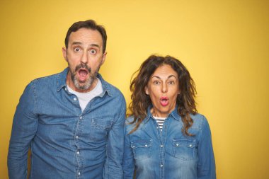 Güzel orta yaş çift birlikte izole sarı arka plan üzerinde ayakta korkuyor ve sürpriz ve hayret ifade, korku ve heyecanlı yüz ile şok.