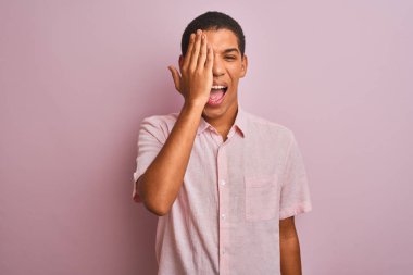 Genç yakışıklı Arap adam rahat gömlek giyerek izole pembe arka plan üzerinde bir göz eliyle kapsayan ayakta, yüzünde kendine güvenen gülümseme ve sürpriz duygu.