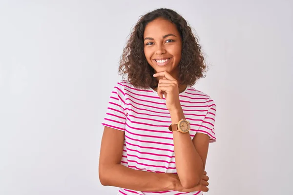 ピンクのストライプのTシャツを着た若いブラジル人女性は 孤立した白い背景の上に立ち 十字架の腕と手をあごに上げて笑顔でカメラに自信を持って見ています ポジティブな考え方 — ストック写真